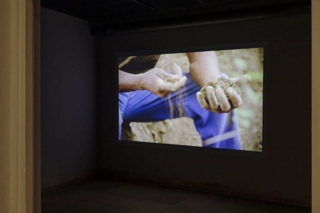 Installationsaufnahme einer Videoprojektion mit Männerhände, die einen Erdbrocken zerbröseln. Cyrill Lachauer, Sammlung Goetz, München