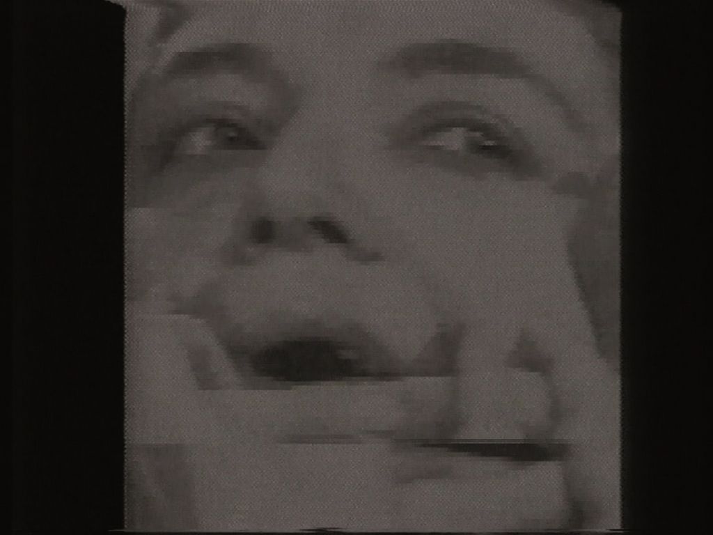 This black and white image detail shows a woman with her mouth open, one half of it held closed by two hands.