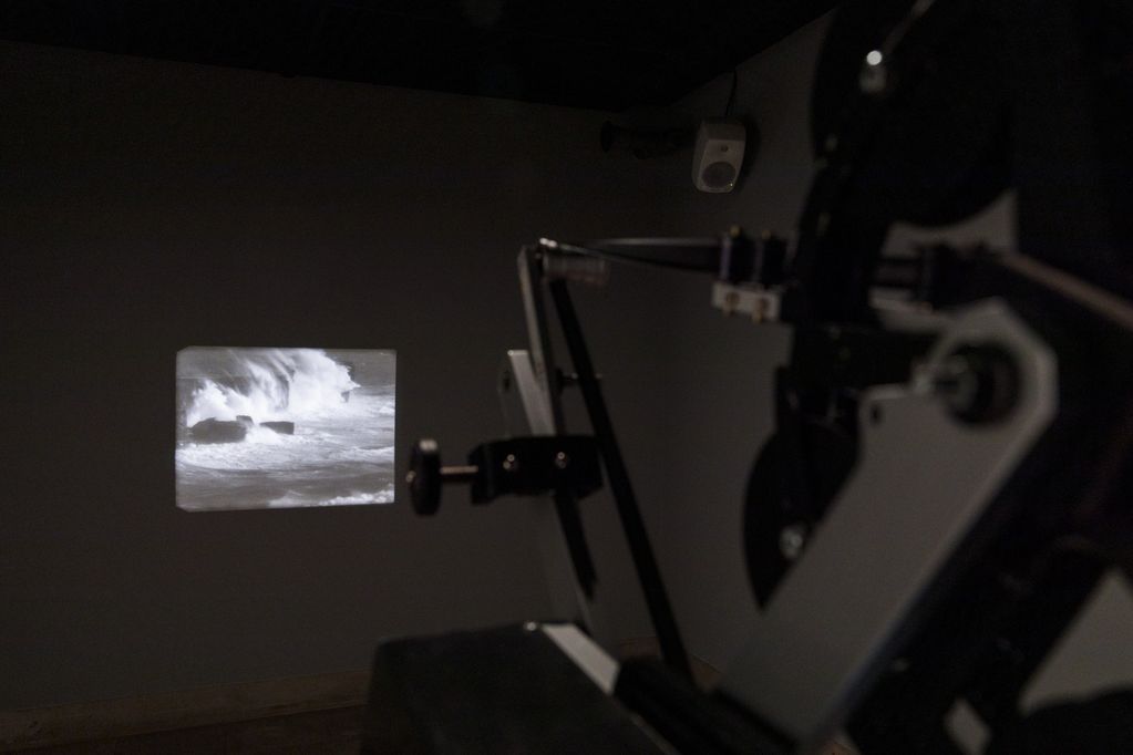 A projector projects a black and white image of breaking waves onto a wall. Cyrill Lachauer, Sammlung Goetz, Munich