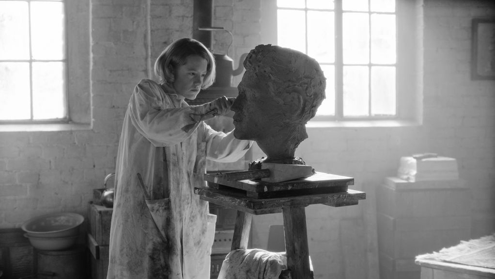 A woman is working on a sculpture that shows a male head 