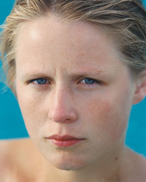 Farbfotografie, Porträt einer jungen blonden, blauäuigigen Frau. Ihre schultern sind nackt und von ihrem Gesciht tropft Wasser. Sie steht vo einem strahlend-hellblauen Hintergrund. Roni Horn, Sammlung Goetz, München  