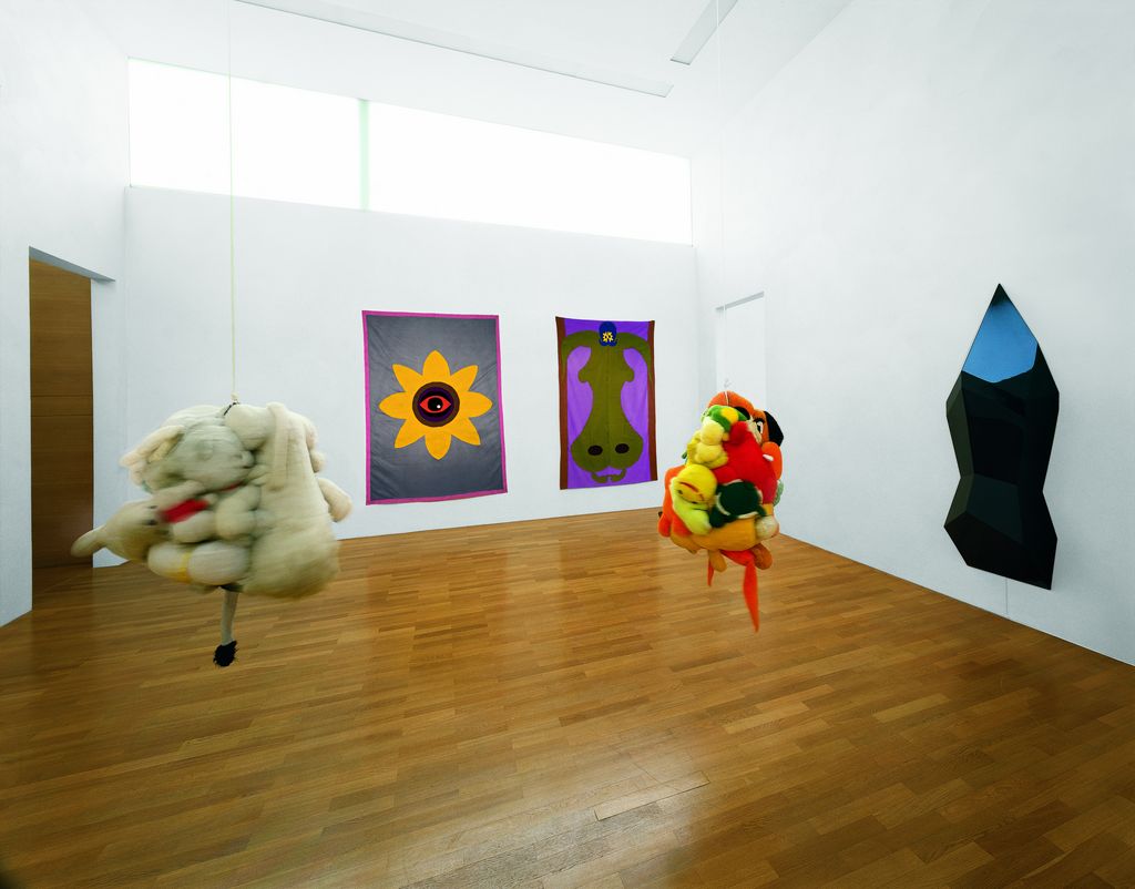 Ausstellungsansicht von zwei Wandteppichen, einem Wandobjekt und zwei von der Decke hängenden Objekten des amerikanischen Künstlers Mike Kelley. Mike Kelley, Sammlung Goetz München