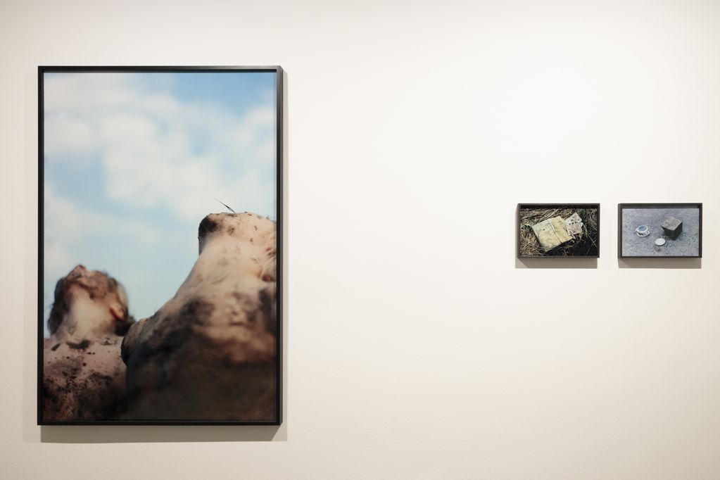 Drei gerahmte Fotografien, links: schlammverschmierte Menschen schauen zum Himmel hoch, rechts zwei kleinformatige Stilleben: Ein Buch und Spielkarten im Heu, ein Topf und ein Teller auf einem gepflasterten Boden. Cyrill Lachauer, Sammlung Goetz, München